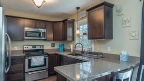 A kitchen with dark wood cabinets, stainless steel appliances, granite countertops, and a window with natural light. - Beary Cozy | Pets, Work Station & 20 Min. from AVL (Black Mountain)