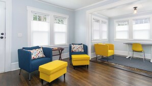 Um quarto com duas poltronas azuis, um banquinho amarelo, uma cadeira amarela e uma mesinha.