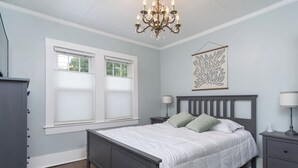 Um quarto com uma cama, duas mesas de cabeceira, um candelabro e uma janela com persianas.