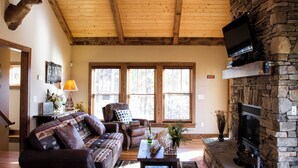 Un salon chaleureux avec une cheminée en pierre, une tête de cerf accrochée au mur et un téléviseur fixé au mur.