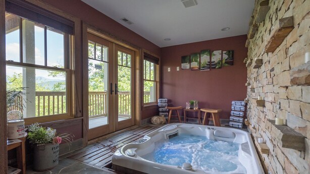 Un espace spa comprenant un bain à remous, une terrasse en bois, des murs en pierre et une vue sur la verdure.
