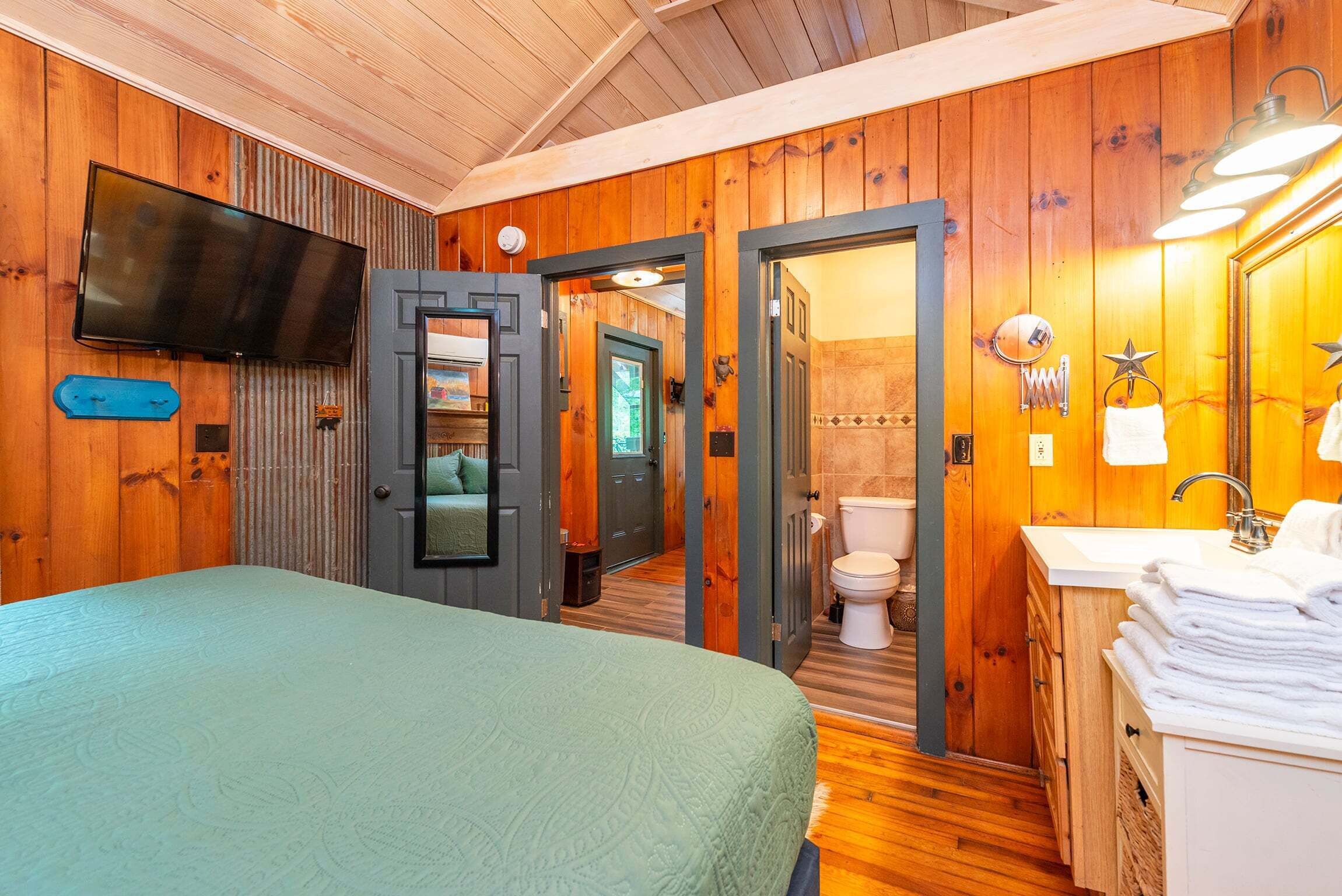 A room with a bed, a television, a bathroom with a toilet, and a sink.