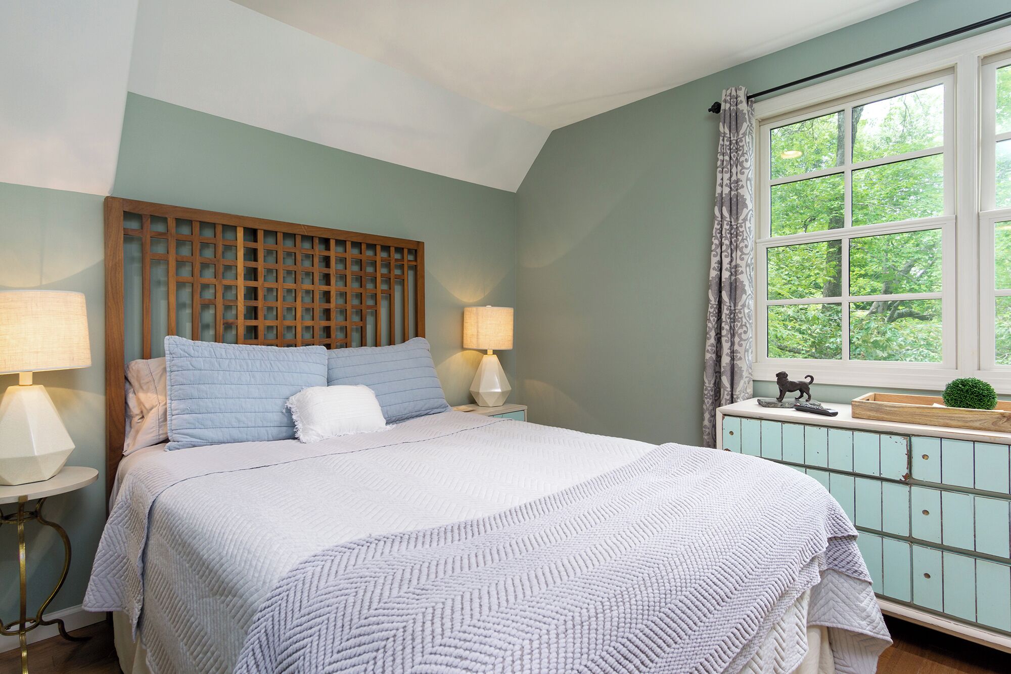 A bedroom with a bed, two bedside tables, a window with curtains, and a dresser.