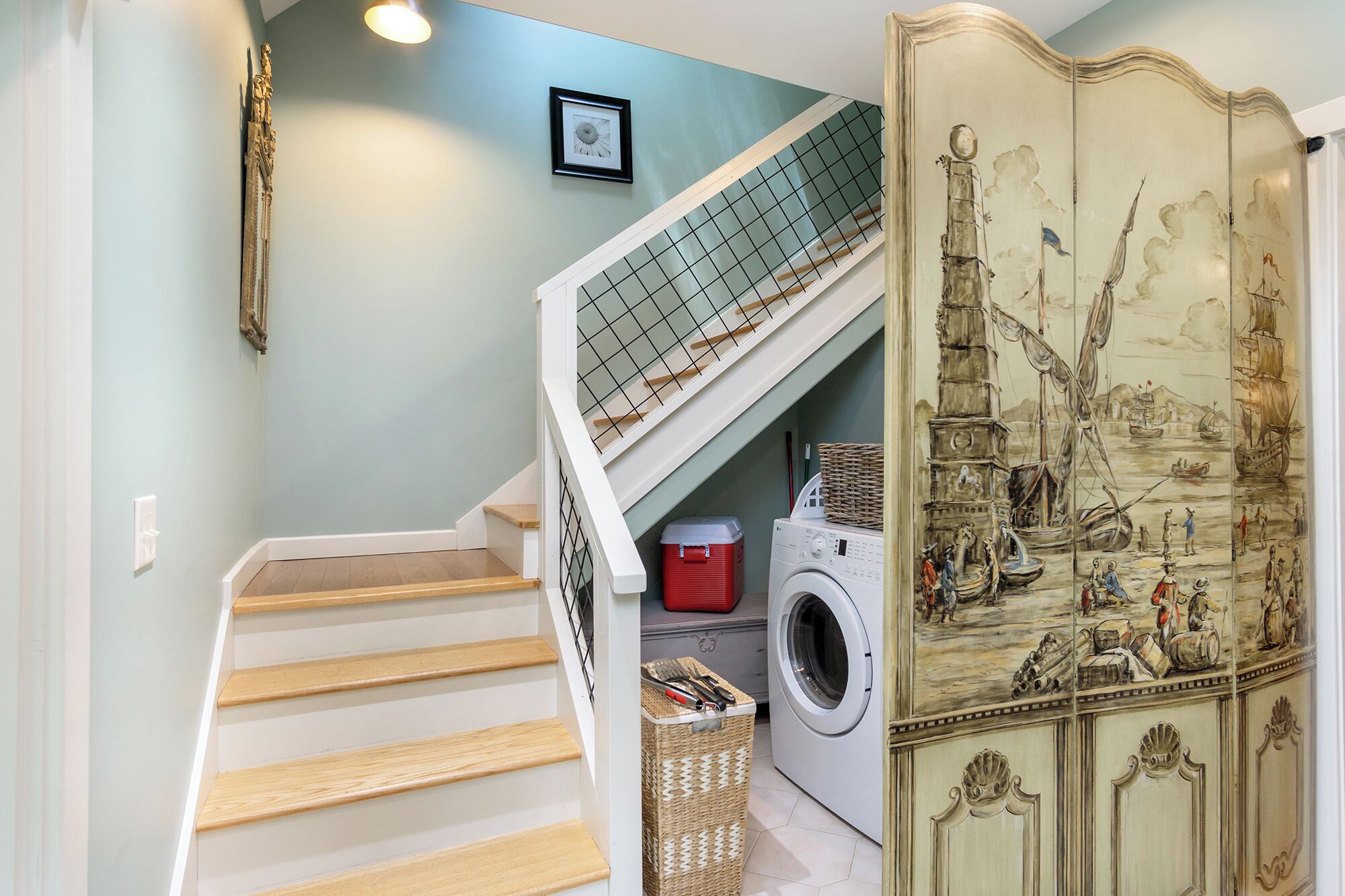 Un escalier avec une rampe en métal menant à une buanderie équipée d’un lave-linge et d’un étendoir.