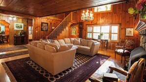 Ein gemütliches Wohnzimmer mit Ecksofa, einer Chandelierleuchte, Holzwänden, einer Treppe und einem Kamin.
