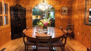 Ein Esszimmer mit Holzwänden, einem runden Tisch, Stühlen, einer Kristallleuchtre und einem Schrank mit Glastüren.