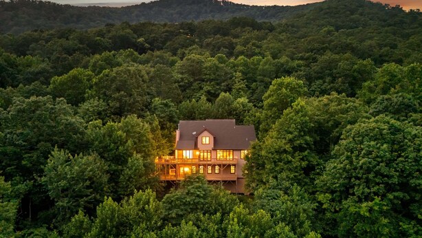 Ein großes, zweistöckiges Haus, umgeben von dichtem Wald, mit einem markanten Balkon und zahlreichen Fenstern.