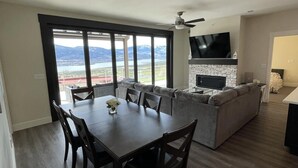 A modern living room with a dining area, a fireplace, and large windows offering a view of the outdoors. - Beautiful Private Residence at Spirit Ridge  (Osoyoos)