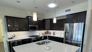 A modern kitchen with dark cabinets, stainless steel appliances, a central island, and pendant lighting. - Beautiful Private Residence at Spirit Ridge  (Osoyoos)