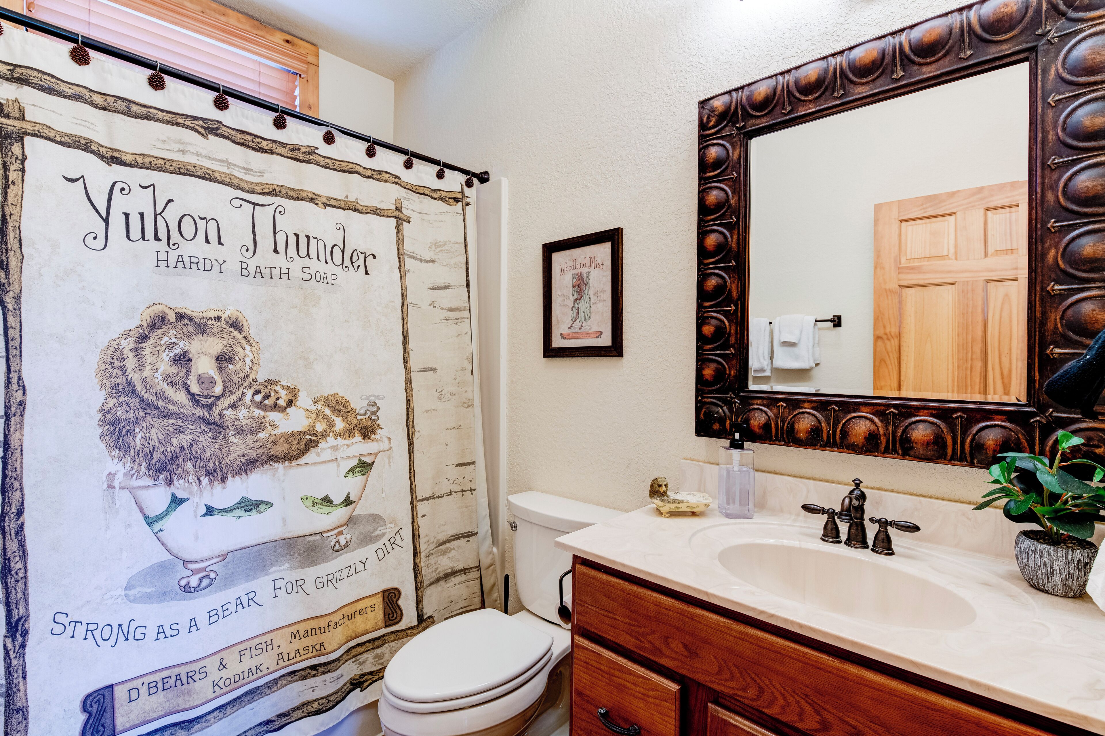 A bathroom with a bear illustration on the shower curtain, a wooden vanity, and a large mirror.