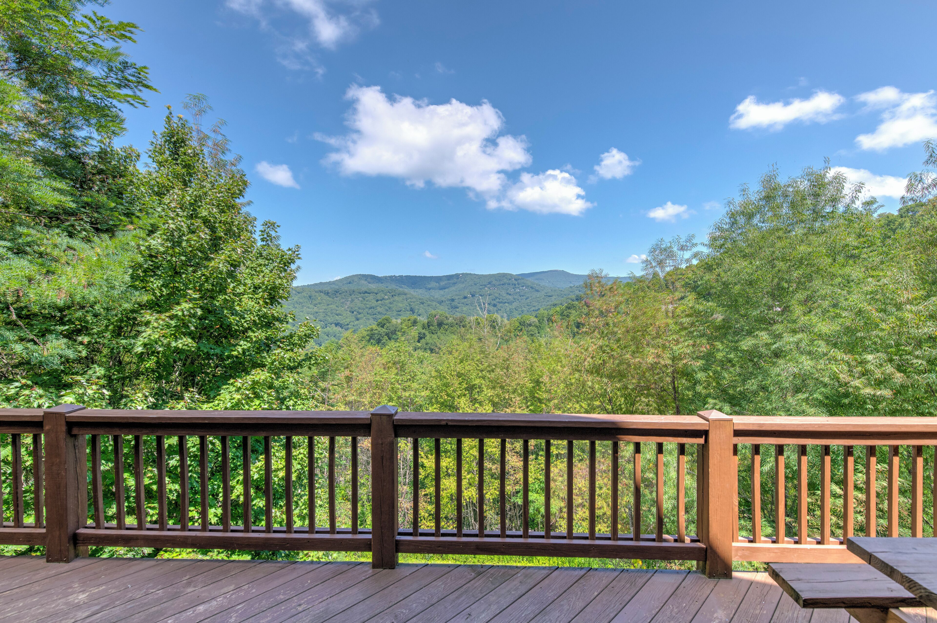 Une terrasse en bois dotée d’une rambarde, qui offre une vue sur un paysage boisé.