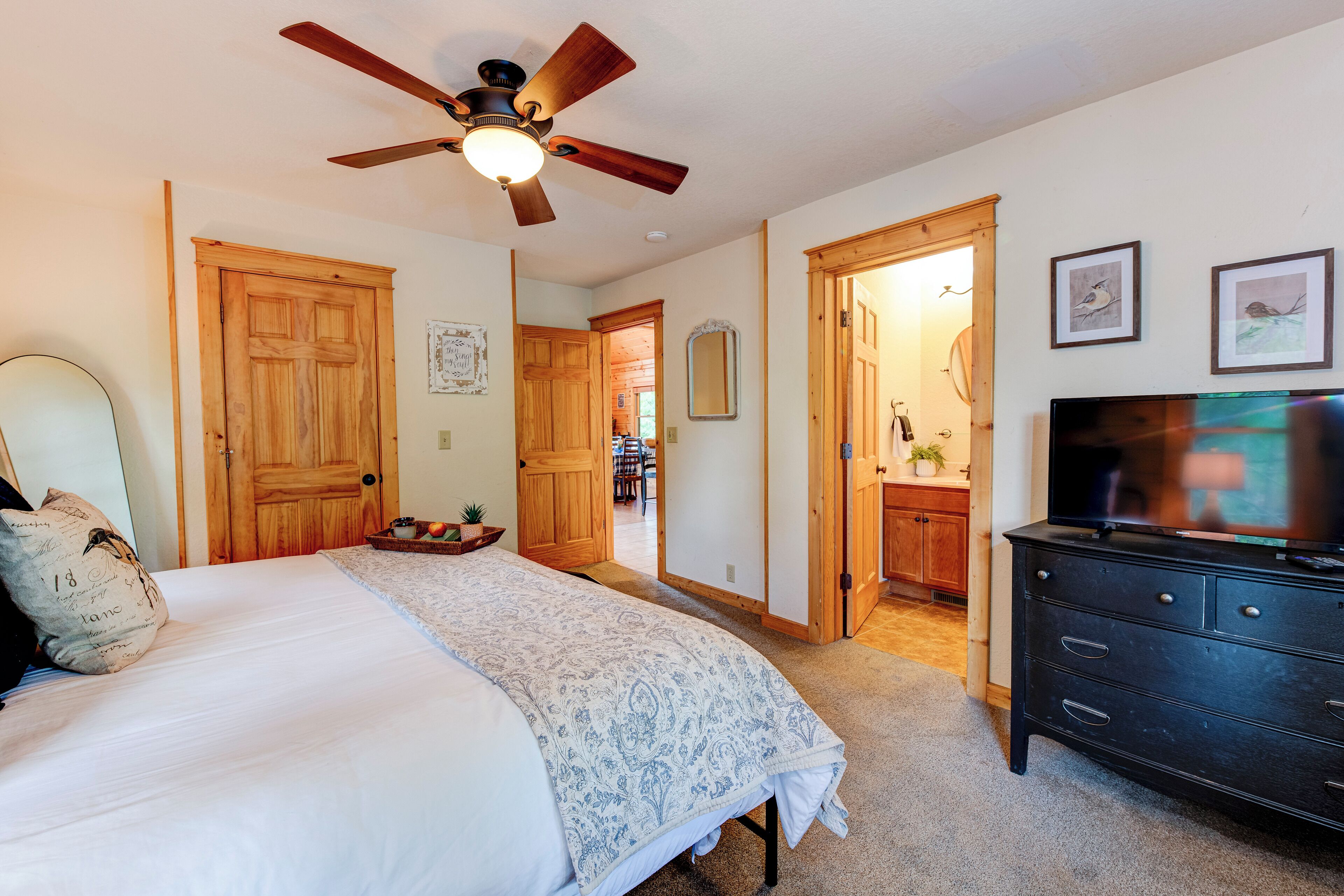 Ein Schlafzimmer mit Bett, Deckenventilator, Holztüren, Kommode und Fernseher.