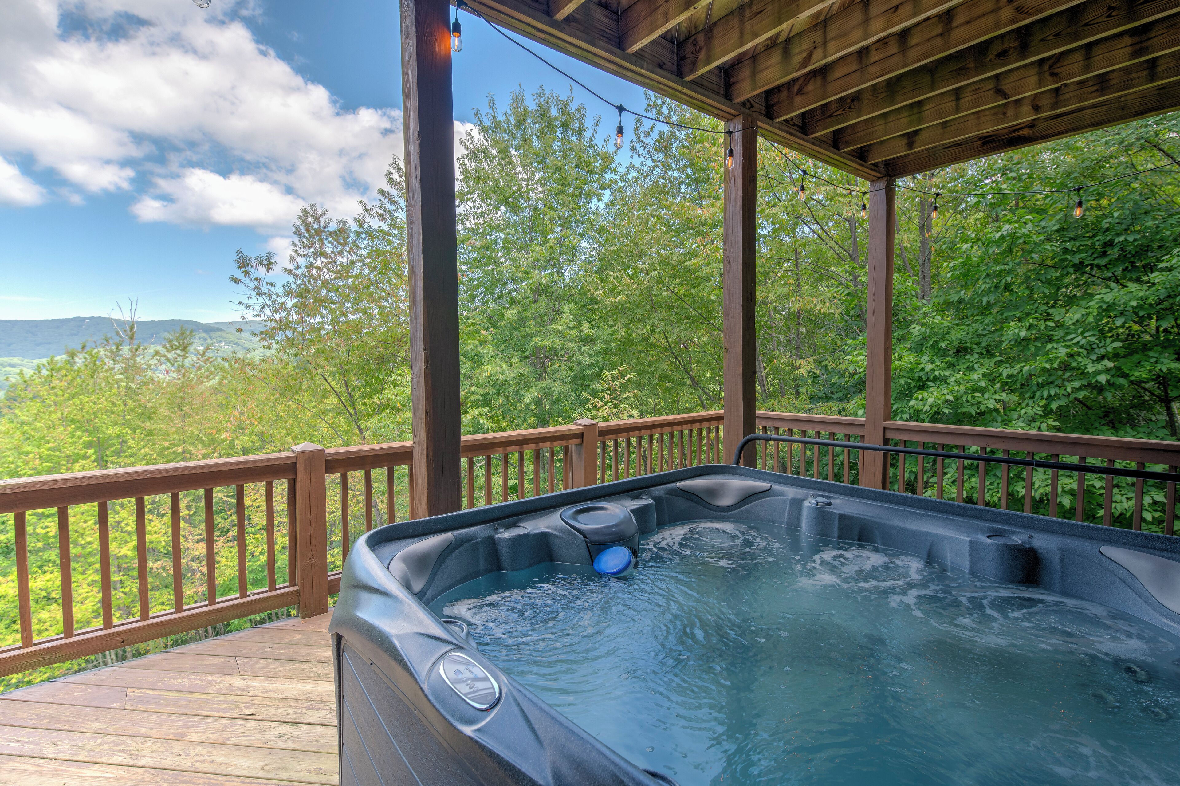 A hot tub on a wooden deck with a view of a forest and mountains.