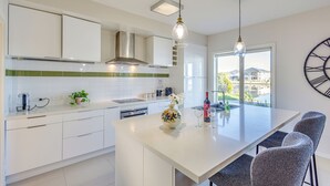 Uma cozinha moderna com armários brancos, uma ilha grande com banquetas, forno embutido e uma janela ampla com vista para a cidade.