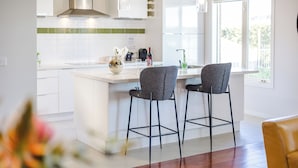 Uma cozinha moderna com armários brancos, painel de fundo verde e dois banquetas.