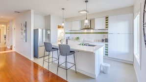 Uma cozinha moderna com ilha central, banquetas, geladeira de aço inoxidável e uma janela que traz luz natural.