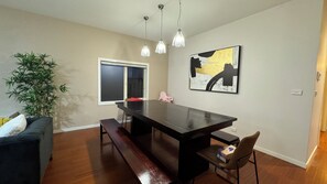 A dining area with a dark wooden table, bench seating, pendant lights, a large window, a potted plant, a couch, and a piece of abstract art on the wall. - StayAU Magnificent Lakefront Villa  (Point Cook)