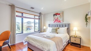 Quarto com uma cama grande, mesa de cabeceira, cadeira e janela com cortinas.