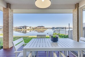 A covered patio with a table and chairs, a potted plant, and a view of a residential area and water body. - StayAU Magnificent Lakefront Villa  (Point Cook)
