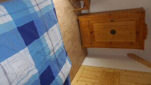 Une pièce avec un meuble en bois, une couverture à carreaux sur le sol et un banc en bois.