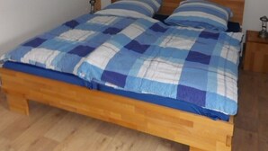 Une chambre à coucher avec un lit en bois, une couvre-lit à carreaux bleus et blancs, et une petite table de chevet avec une lampe.