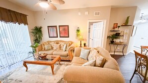 A living room with a sofa, coffee table, and a dining area with a table and chairs. - Budget Friendly Condo in Windsor Hills Resort w garden view (Kissimmee)