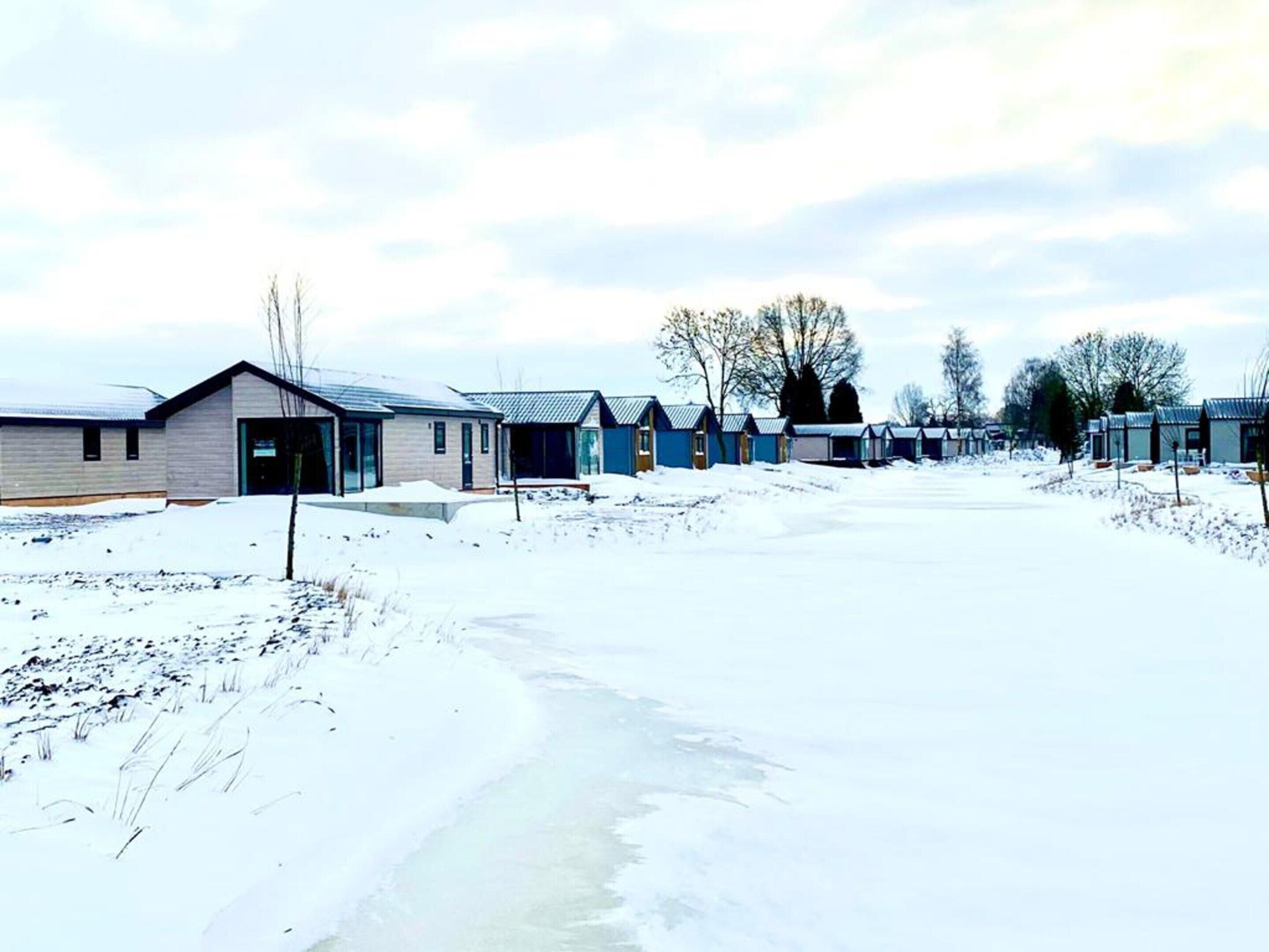 Een rij laagbouwgebouwen met grote ramen, waarschijnlijk een motel of camping, in een besneeuwd landschap.
