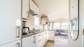 Cozinha moderna com eletrodomésticos de aço inoxidável, cafeteira e janela com vista para uma sala de estar com sofá e mesa.