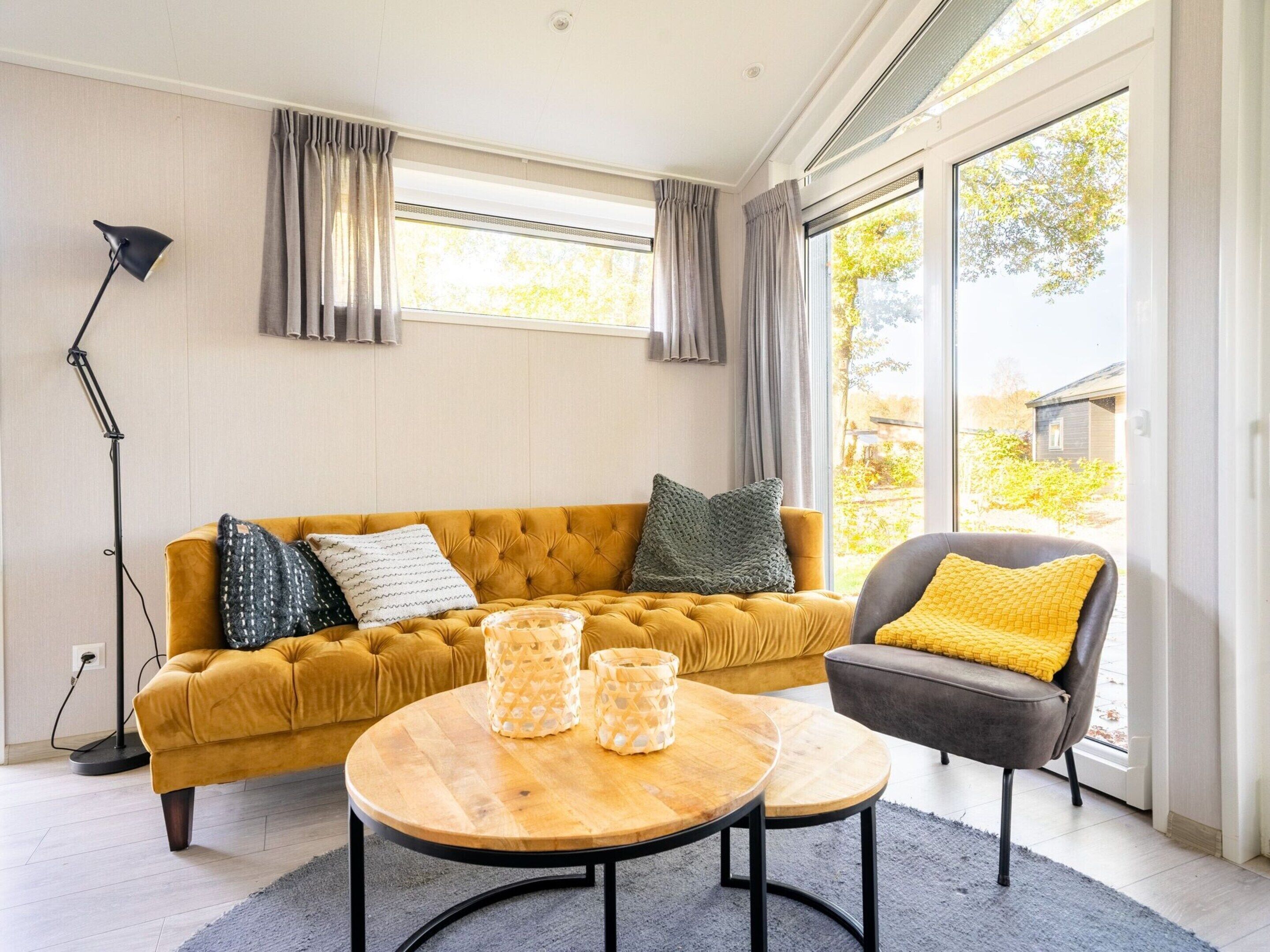 A modern living room with a mustard-colored sofa, a dark armchair, and a wooden coffee table.