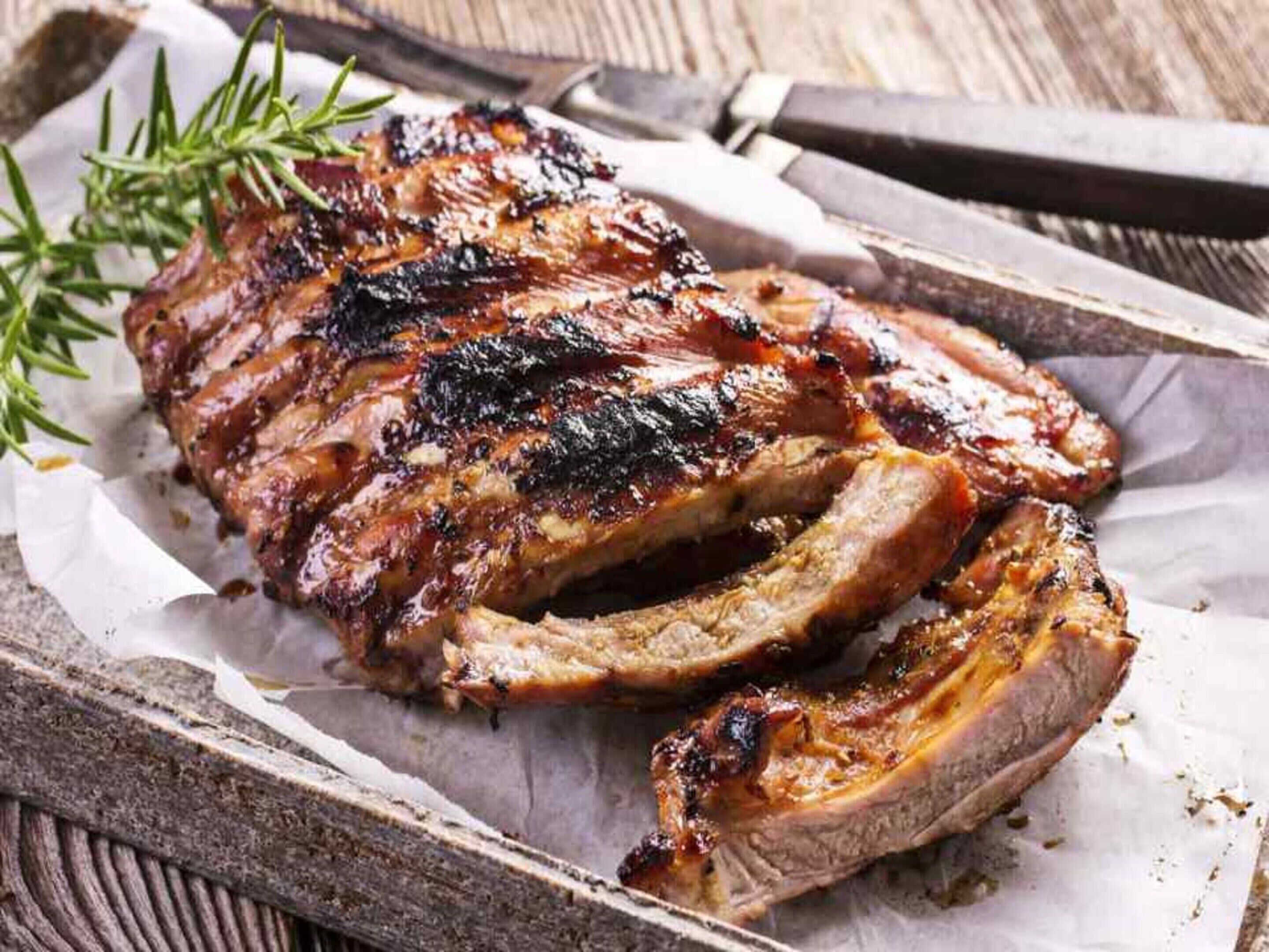 A rack of ribs on a wooden tray with a sprig of rosemary.