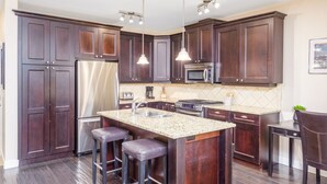 Una cocina con alacenas de madera oscura, electrodomésticos de acero inoxidable, encimera de granito y un taburete de bar.