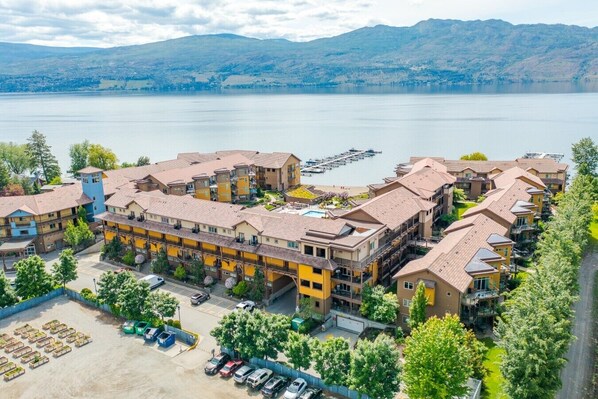 A multi-story hotel with a central courtyard, surrounded by a body of water and mountains in the background.
