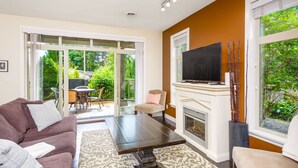 Una sala de estar con sofá, mesa de centro, chimenea, televisor y puerta corrediza de vidrio que da a un patio con mobiliario exterior.