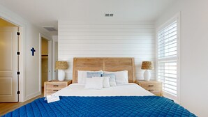 Un dormitorio con una cama grande, cabecera de madera, dos mesitas de noche con lámparas y una ventana con persianas.