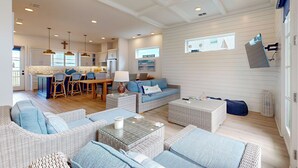 Un amplio salón con muebles de mimbre, un comedor y una cocina al fondo.