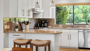 Una cucina moderna con mobili bianchi, un piano di lavoro in granito, un piano cottura integrato e una finestra vista verde.