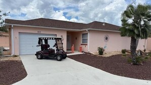 A single-story house with a garage, a golf cart parked in front, and a palm tree. - 2 bed/2bath Courtyard Villa Spanish Springs w/cart (The Villages)