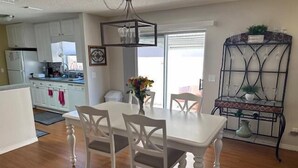 A modern kitchen with white cabinets, a dining area with a white table and chairs, and a decorative metal shelf with glassware. - 2 bed/2bath Courtyard Villa Spanish Springs w/cart (The Villages)