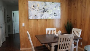 Een eetgedeelte met een wand van houten panelen, een donkerhouten tafel en witte stoelen.