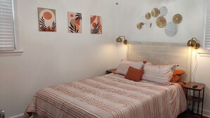 Een slaapkamer met een bed, twee nachtkastjes, decoratieve muurkunst en een raam met zonwering.