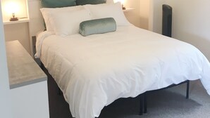 Un lit bien fait, avec une literie blanche et verte, un élément décoratif accroché au mur au-dessus, et un ventilateur de plafond.