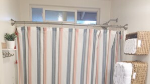 Une salle de bain avec un rideau de douche à rayures, des toilettes, un lavabo blanc et une petite étagère contenant des articles de toilette.