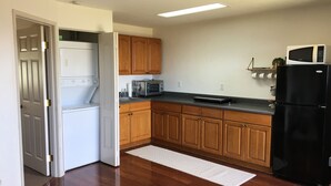 Une cuisine avec des meubles de rangement en bois, un réfrigérateur noir, un four à micro-ondes, un grille-pain et un lave-linge.