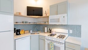 A compact kitchen with white cabinets, a microwave, a gas stove, and a herringbone-patterned backsplash. - Cozy, walkable 1-bedroom apartment in Pittsburgh with WiFi, AC (Pittsburgh)