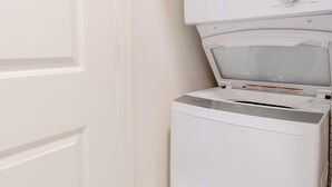 A compact laundry room with a washing machine and dryer, a white door, and a green detergent bottle. - Cozy, walkable 1-bedroom apartment in Pittsburgh with WiFi, AC (Pittsburgh)