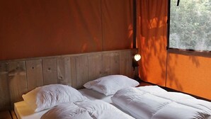 Ein Zimmer mit zwei Betten, einem Holzkopfende, weißer Bettwäsche, einem Nachttisch und einem Fenster mit Vorhängen.