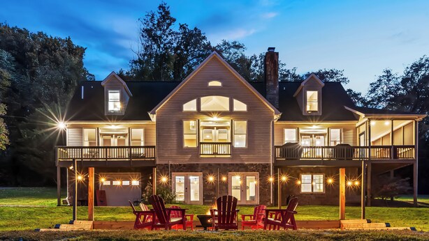 A two-story house with a balcony on the upper floor, a fire pit in the front yard, and red Adirondack chairs. - Stunning Views, Riverfront Privacy, 18-Acre Estate - Near Hikes, Wine/Breweries! (Charles Town)