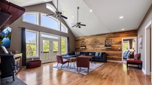 A spacious living area with a high ceiling, large windows, and a wooden accent wall. - Stunning Views, Riverfront Privacy, 18-Acre Estate - Near Hikes, Wine/Breweries! (Charles Town)