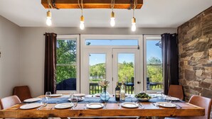 A dining area with a wooden table set for six, large windows, and a stone wall. - Stunning Views, Riverfront Privacy, 18-Acre Estate - Near Hikes, Wine/Breweries! (Charles Town)