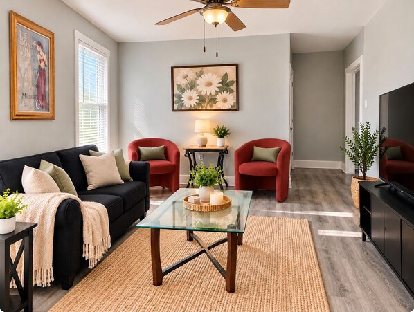 A living room with a black sofa, red armchairs, a glass coffee table, and a ceiling fan.